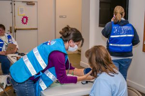 Three MRC volunteers, wearing blue MRC vests checking blood pressure.